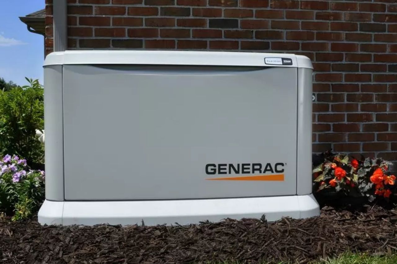 A grey generator set on brown mulch against brick style building