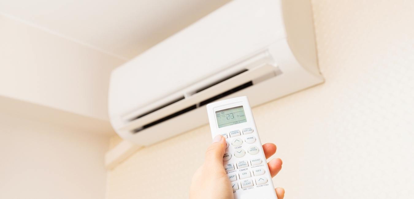 A hand holding a remote pointed at ductless AC unit in wall