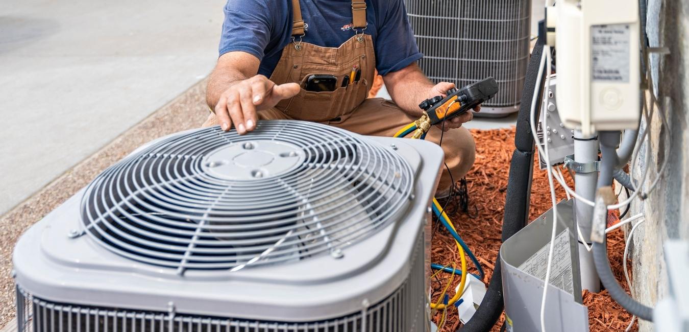 A technician's hand over an air conditioning unit with a tester in the other hand