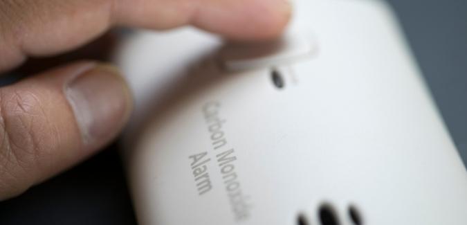 A finger pressing button on a white CO detector unit