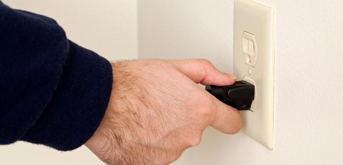 A hand unplugging a power cord from a wall outlet