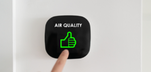 A finger pointing at a air quality testing device with a green thumbs up icon and a black background