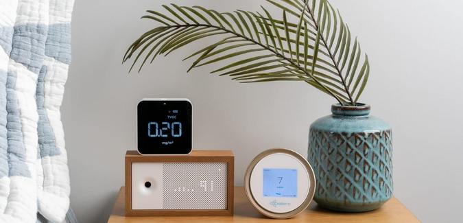 Different air quality monitoring devices on top of a wood night stand next to a bed
