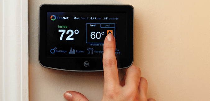 A woman's hand pushing setting on Smart Thermostat unit Mounted on a beige color wall