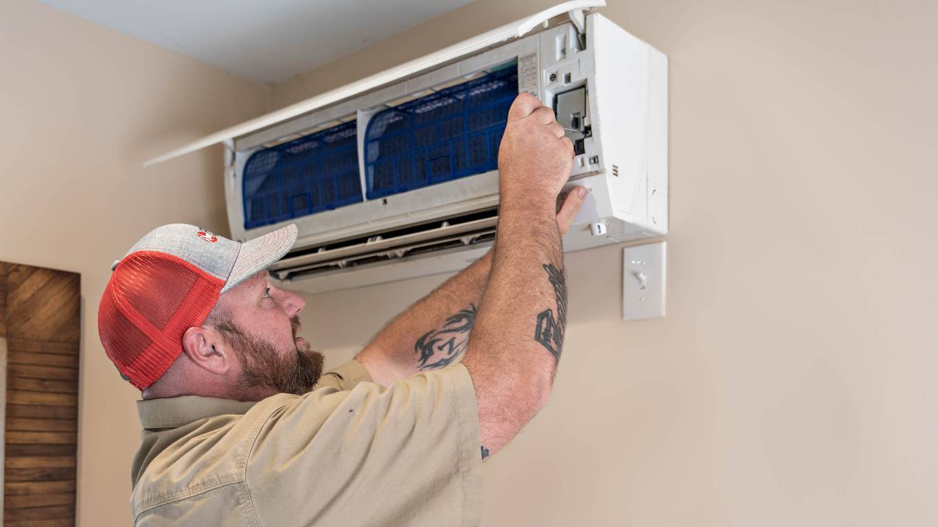HVAC Service technician inspecting air conditioning unit in the wall of a home